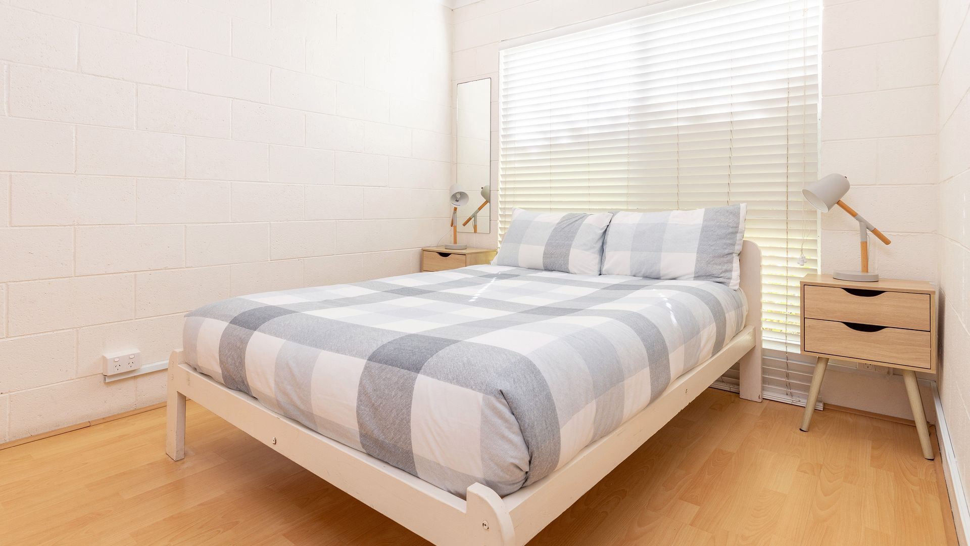 A bedroom with a bed, bedside tables, a lamp, and a window with blinds.