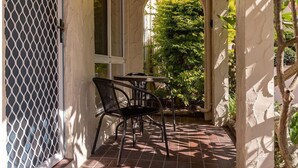 A covered patio with a tiled floor, a table and chairs, and a view of greenery through an archway.