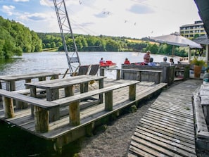 Une jetée en bois avec des bancs, un petit bateau et un bâtiment surmonté d’un parasol.