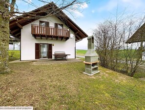 A two-story house with a balcony, a stone oven, and a bench in the yard.