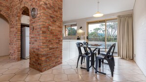 A modern kitchen with a brick wall, a dining area with a glass table and chairs, and a large window with curtains.