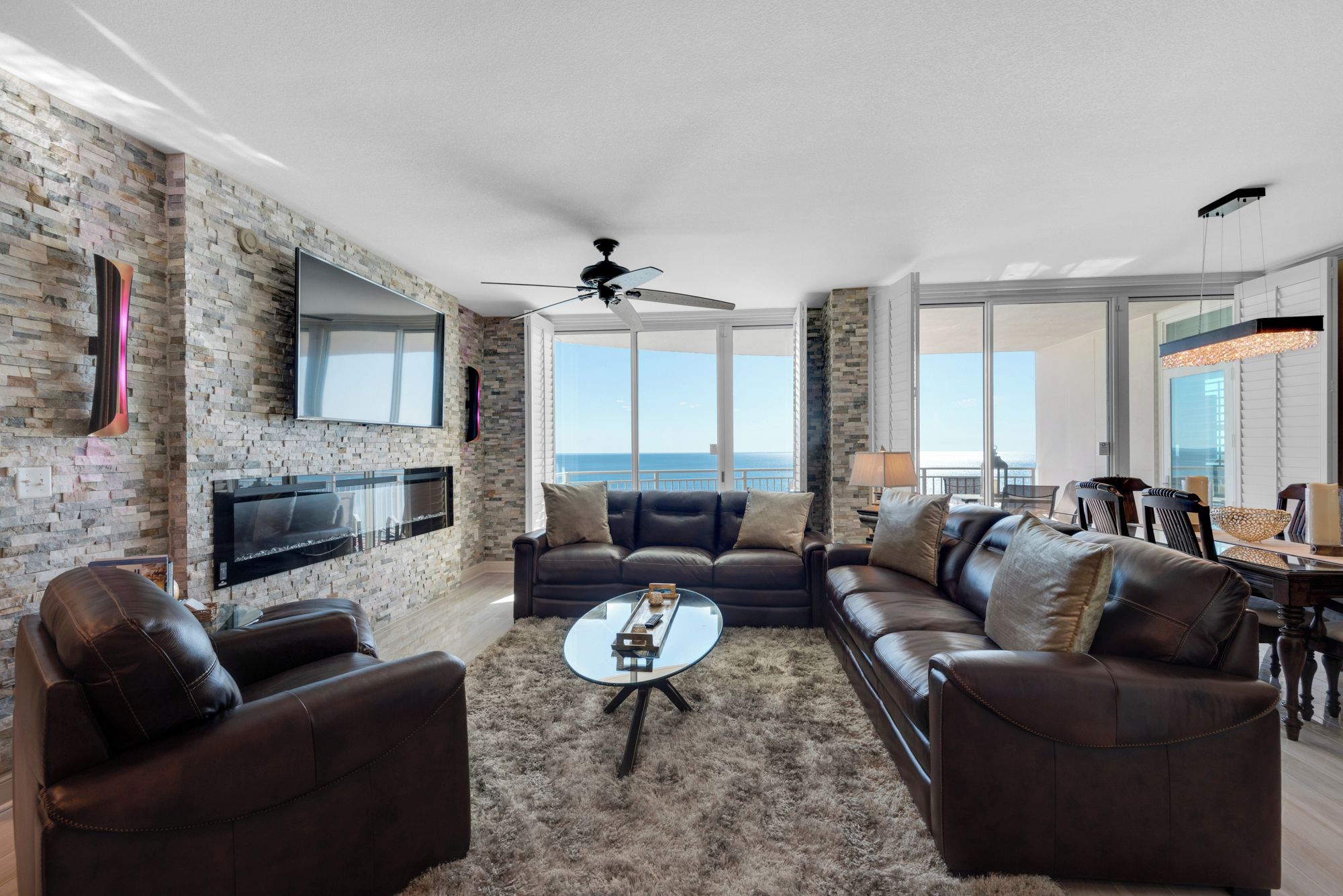 A spacious living room with a large sectional sofa, a coffee table, and a flat-screen TV mounted on a brick wall.