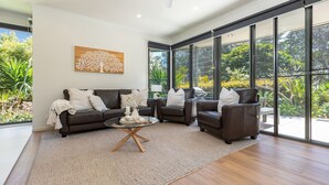 A modern living room with a dark brown sofa set, a glass coffee table, and a large window offering a view of greenery. - Boom 8 - Boomerang Beach (Boomerang Beach)