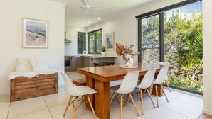 A modern kitchen with a dining area, large windows, and a view of greenery. - Boom 8 - Boomerang Beach (Boomerang Beach)