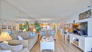 A living room with a sofa, coffee table, TV, and a dining area with chairs and a table. - XPLORIE ACTIVITIES & LINENS INCLUDED*! Spacious and upgraded 3BR/2BA Plaza condo. (Ocean City)