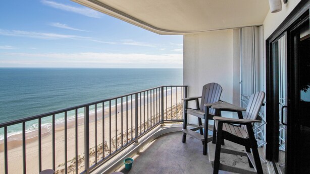 A balcony with a view of the ocean, a table, two chairs, and a small bucket. - XPLORIE ACTIVITIES & LINENS INCLUDED*! Spacious and upgraded 3BR/2BA Plaza condo. (Ocean City)
