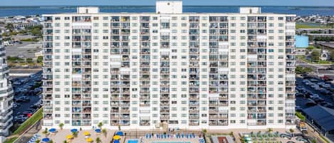 A high-rise hotel with multiple balconies, a swimming pool, and a parking area.