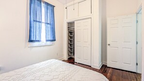 A bedroom with a bed, a window with curtains, a closet with shelves, and a door. - Funky Home Away from Home  (New Orleans)