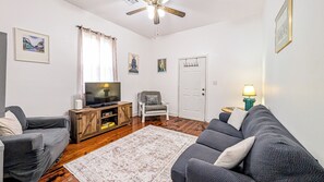 Ein Wohnzimmer mit Fernseher, zwei Sofas, einem Sessel, einem Teppich und einem Deckenventilator.