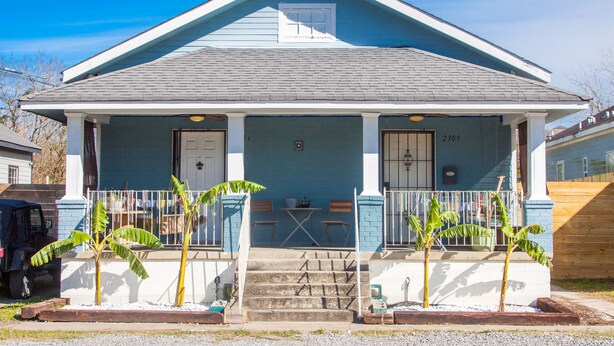 A two-story house with a porch, a garage, and a small front yard with banana plants. - Funky Home Away from Home  (New Orleans)