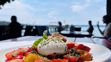 A plate of food with a white sauce and tomatoes, set on a table with a view of the sea.