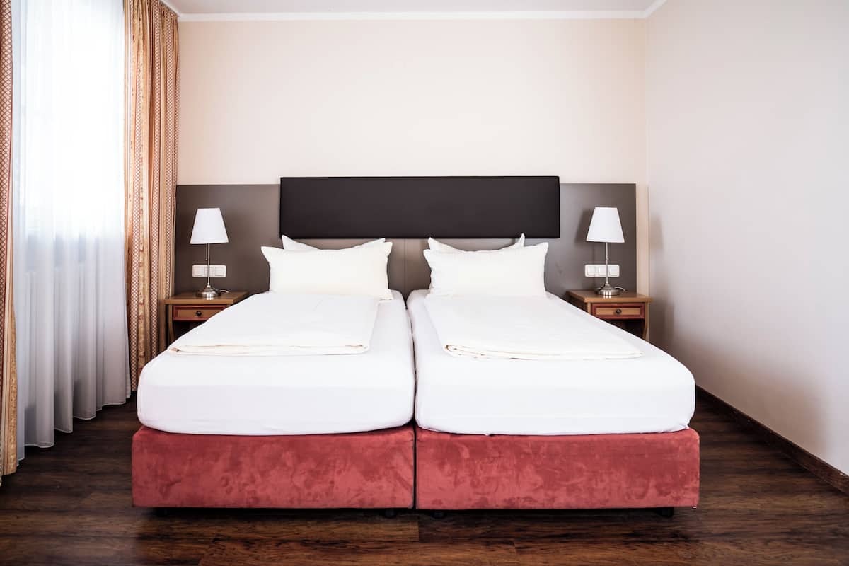 Una cama doble con cabecera, dos mesitas de noche con lámparas y un ventanal con cortinas.