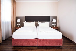 Una cama doble con cabecera, dos mesitas de noche con lámparas y un ventanal con cortinas.