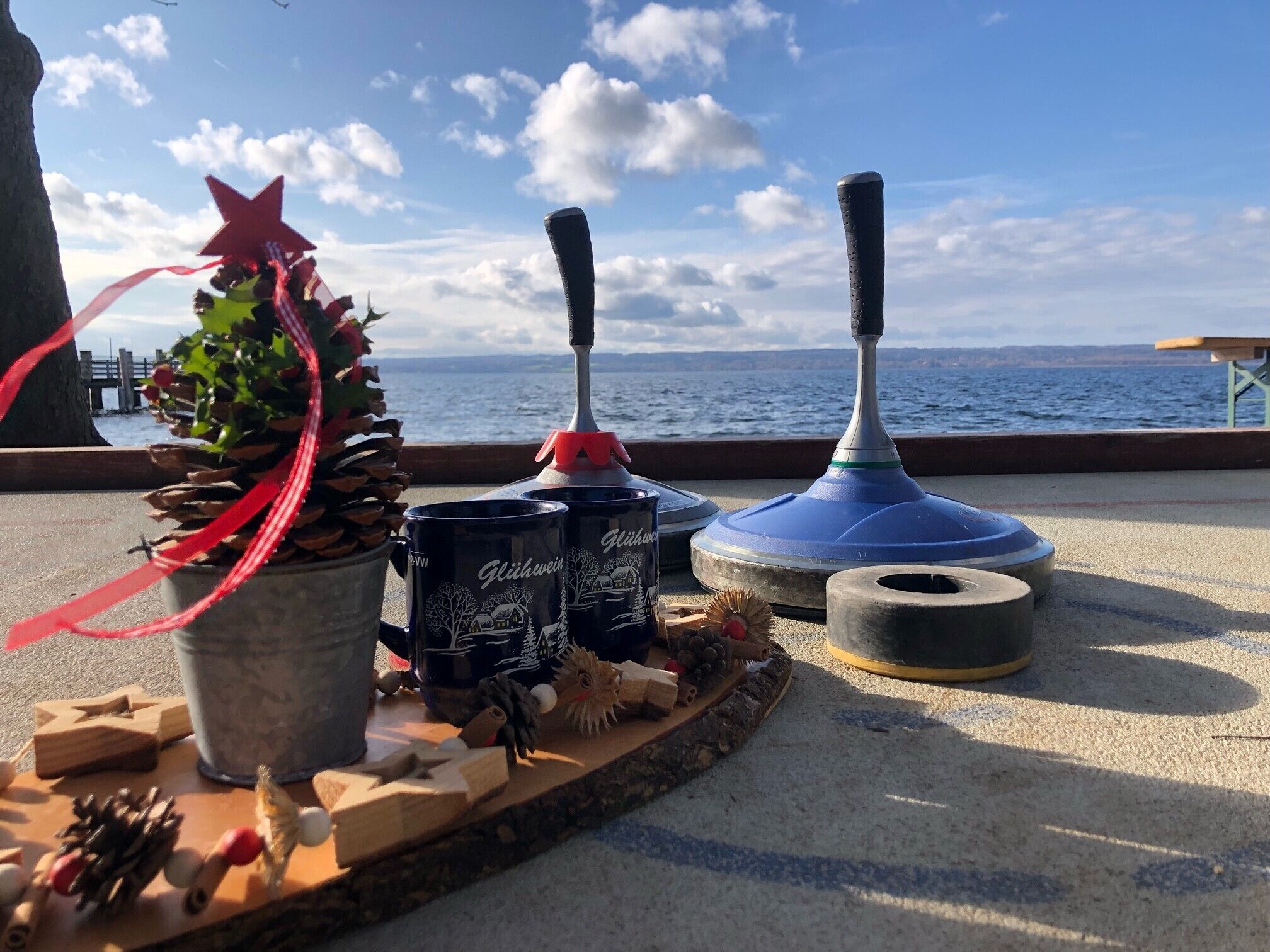 Una mesa con una planta en maceta, dos tazas, un juguete de madera y un objeto azul en una terraza con vistas al mar.