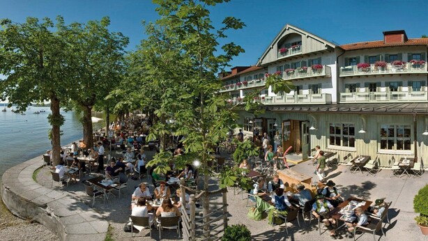 Ein See-Restaurant mit Terrassenbereich, umgeben von Bäumen und einem Gebäude mit Balkonen.