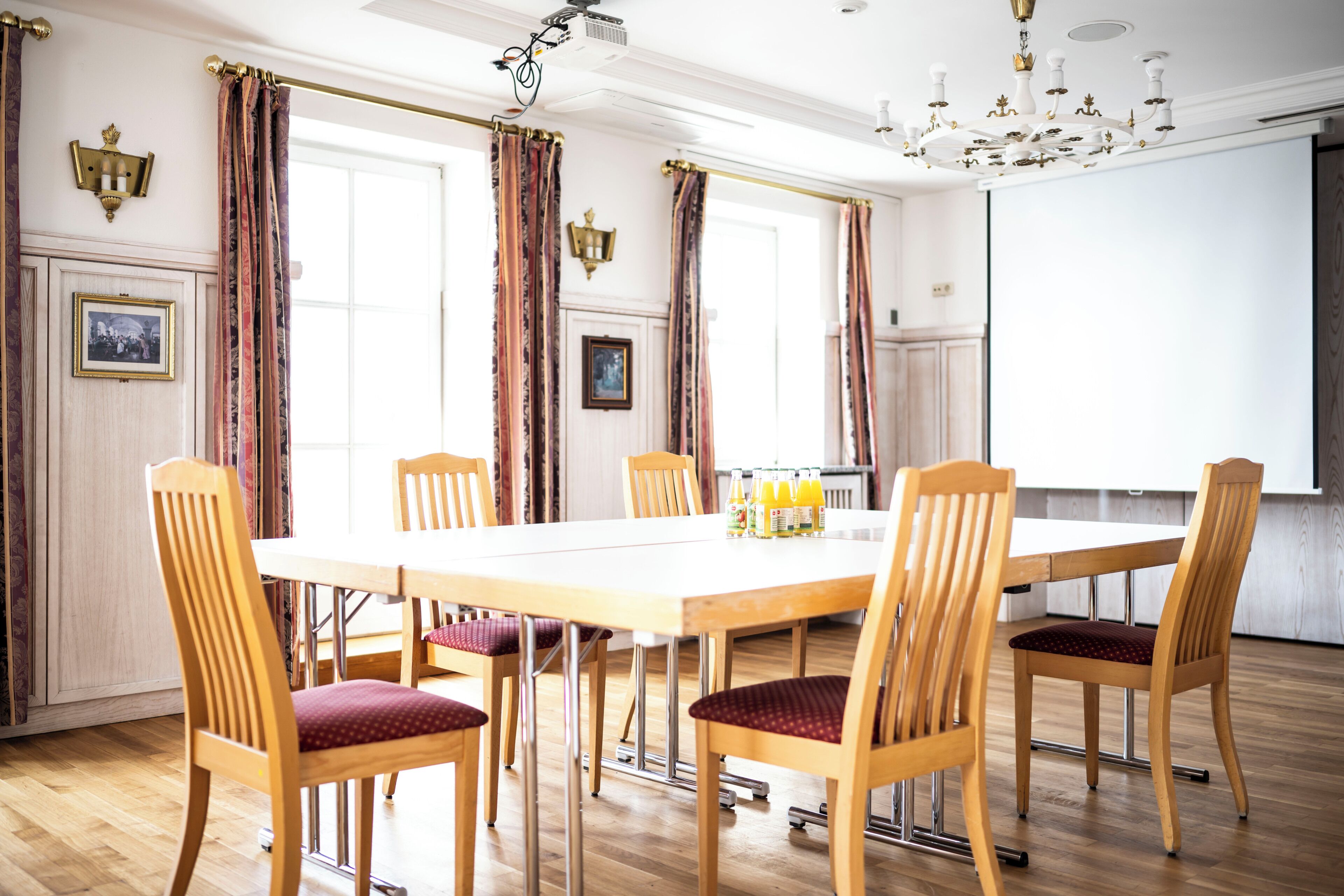 A dining area with a long table, wooden chairs, and a projector screen.