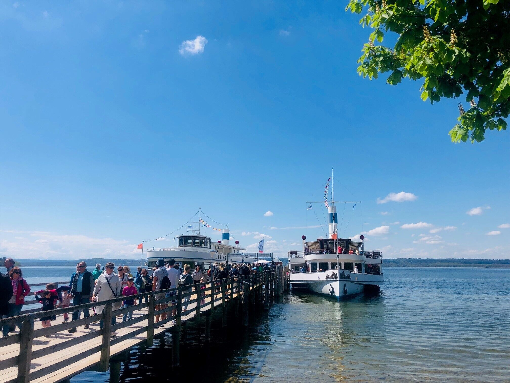 A pier with people walking, two boats docked, and a clear sky.