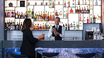 A bar area with a bartender and a customer, shelves of various liquor bottles, and bar stools.