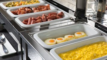 Buffet com diversas opções de comida, incluindo cachorros-quentes, ovos e ovos mexidos.