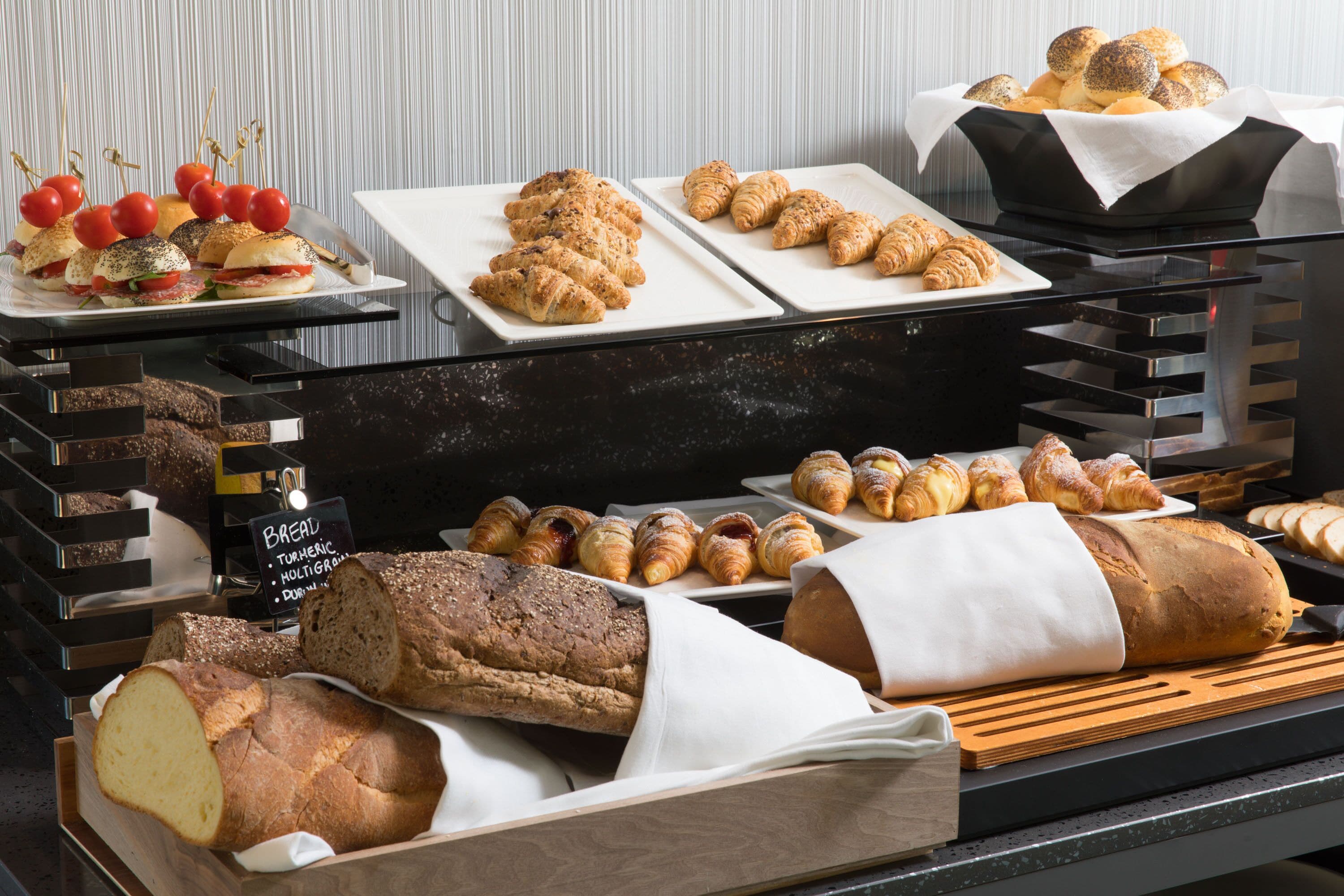 Variedad de productos horneados, incluyendo pan, croissants y pastelería, exhibidos en una mesa de buffet.
