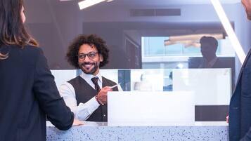 A reception desk with a modern design, a person standing behind it, and a counter with a glass partition.