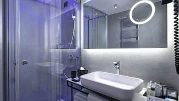 Un baño moderno con cabina de ducha de vidrio, un lavabo blanco y tocador con artículos de aseo.
