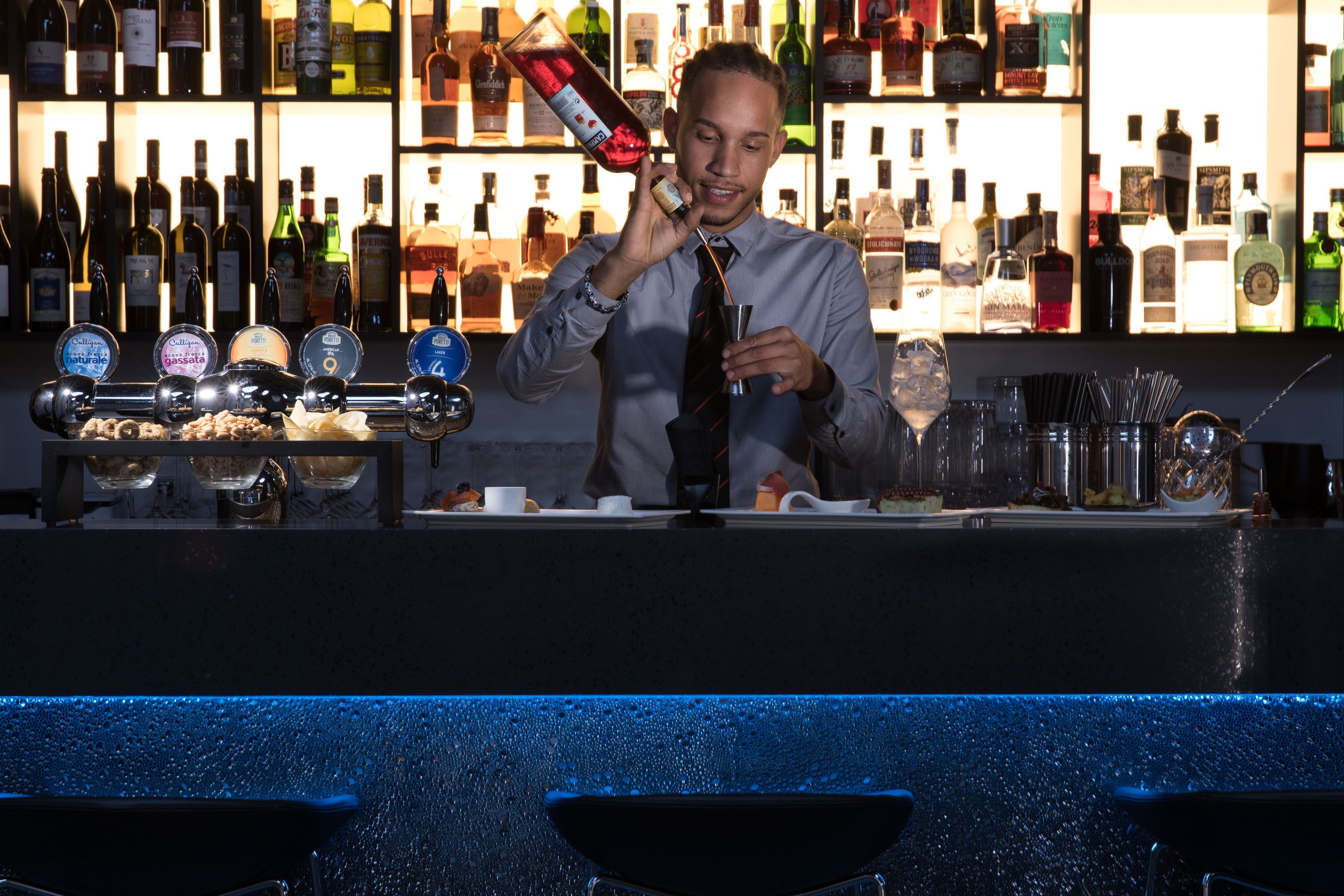 A bartender preparing a drink behind a bar with various bottles and glasses.