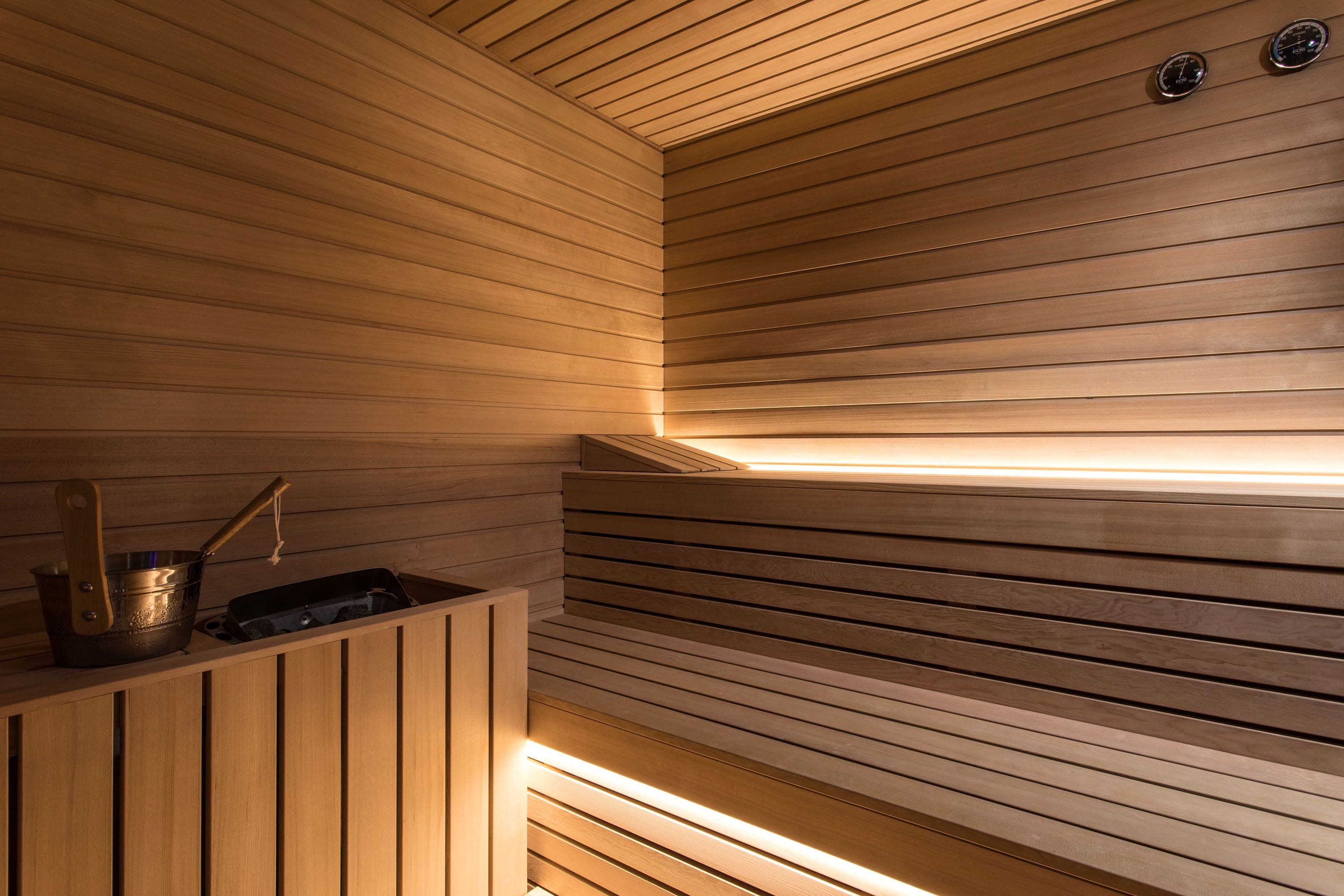 A sauna with wooden slats and a bench, a metal bucket, and a wooden cabinet.