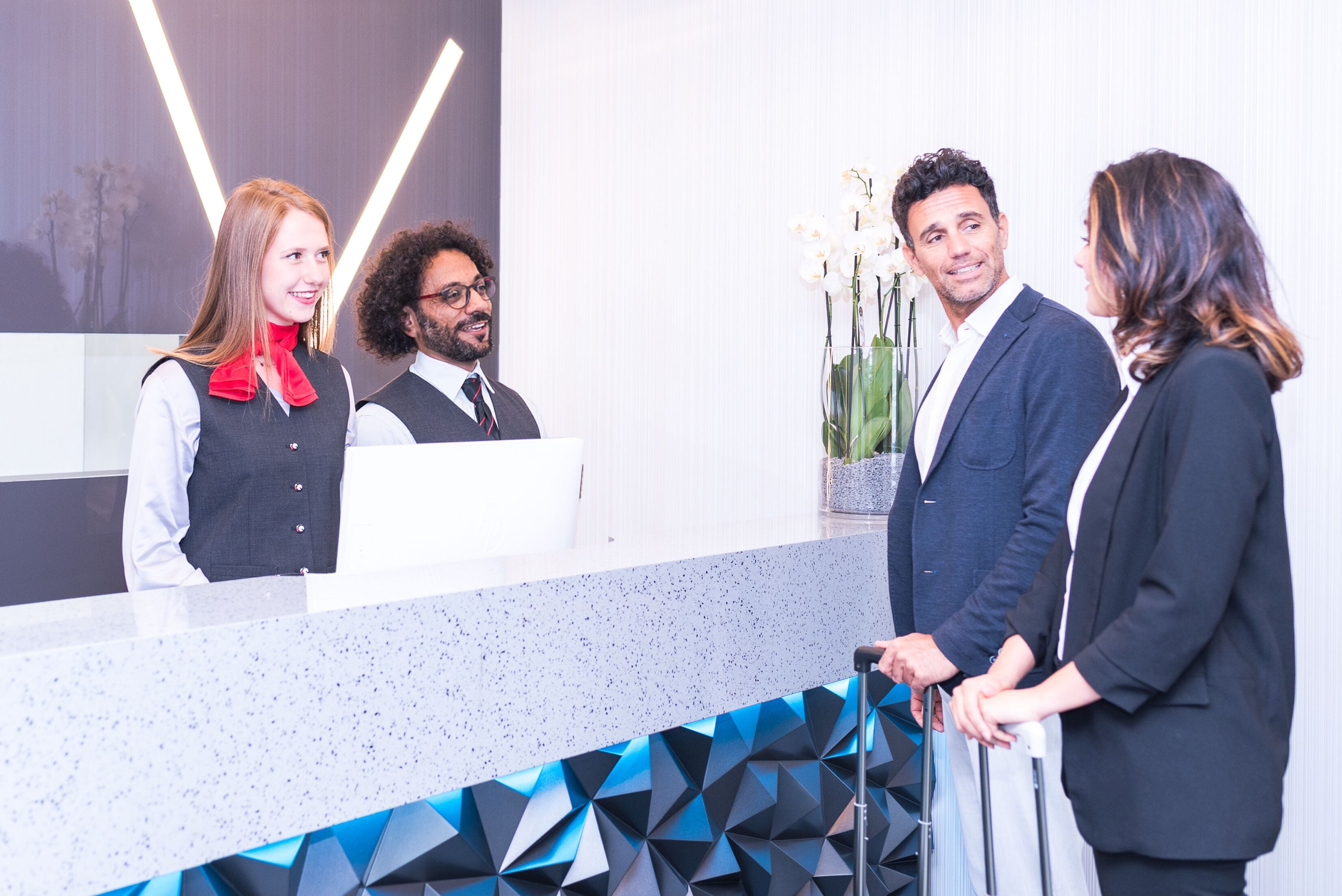 A reception desk with a modern design, a digital screen, and a vase with flowers.