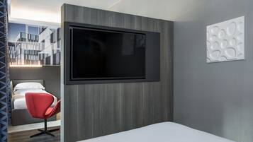 A modern hotel room with a large flat-screen TV mounted on the wall, a red chair, and a bed.
