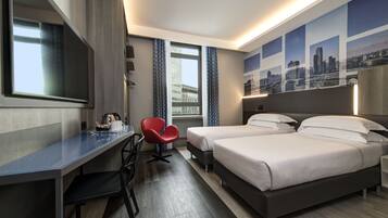 Habitación de hotel con escritorio, dos camas, una silla roja, un ventanal grande y una obra de arte con motivos urbanos en la pared.