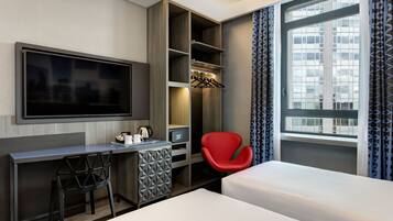 A hotel room with a bed, a desk with a chair, a TV, and a window with curtains.