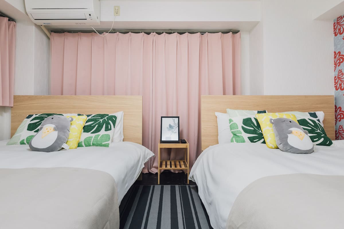 A hotel room with two beds, each with a wooden headboard, white bedding, and decorative pillows. There is a small wooden nightstand with a framed picture between the beds.