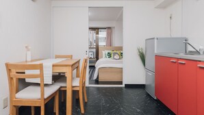 A compact room with a dining table, chairs, a bed, a kitchenette, and a bathroom visible through an open door. - AFP Shimanouchi J Apartment (Osaka)