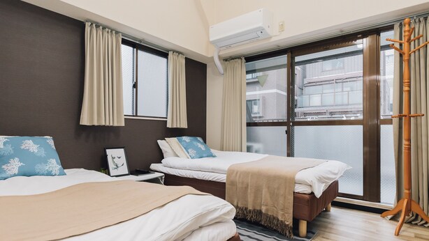 A hotel room with two beds, a large window, an air conditioning unit, and a wooden floor. - AFP Shimanouchi J Apartment (Osaka)