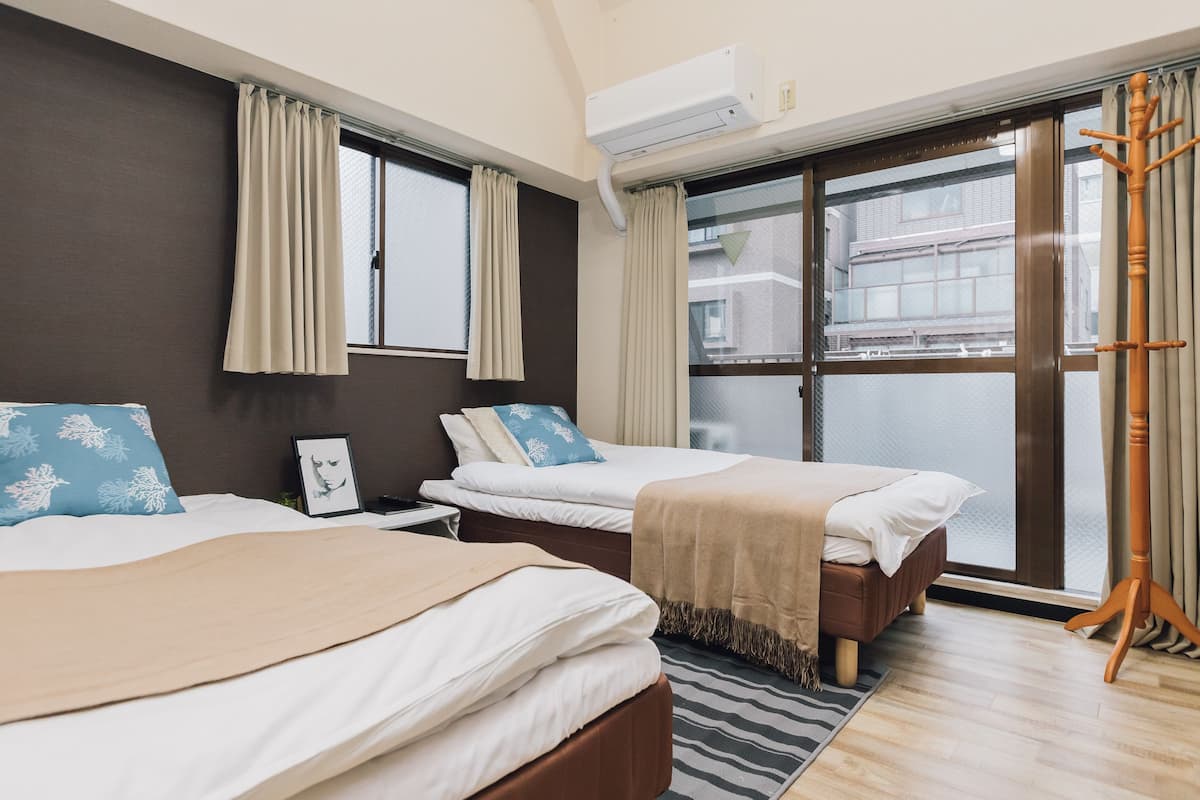 A hotel room with two beds, a large window, an air conditioning unit, and a wooden floor.