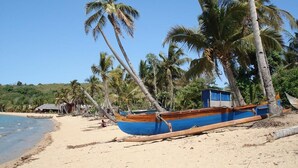 A beach with a blue boat tied to a palm tree, a small blue structure, and a sandy shore.