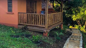 A small house with a thatched roof and wooden balcony, surrounded by greenery.