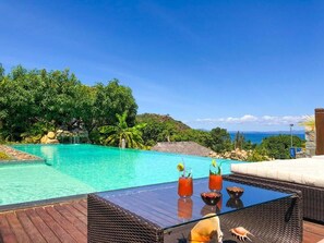A poolside area with a glass table, two drinks, and a tropical view. - Jj Et Euphrasie (Nosy Be)