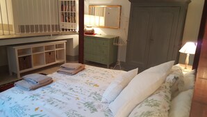 Ein Schlafzimmer mit Bett, Nachttisch, Kommode, Spiegel, Kleiderschrank und einem Regal mit Büchern.