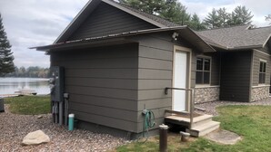 Une petite cabane à un seul étage, avec une porte d’entrée, un petit porche et une jetée qui s’avance dans un lac.