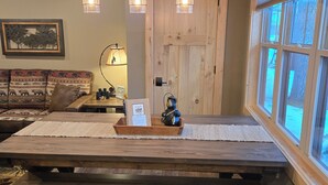 Une table à manger rustique en bois, avec des bancs, une porte en bois et une fenêtre avec des stores.