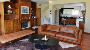 A living room with a brown leather sofa, a black coffee table, and a fireplace. There is a kitchen visible through an open doorway. - Villa Xenia (Saronikos)