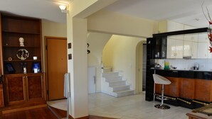 A spacious kitchen with a wooden cabinet, a white refrigerator, and a bar area with stools. - Villa Xenia (Saronikos)