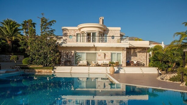 Ein großes, luxuriöses Haus mit Swimmingpool, umgeben von Palmen und blauem Himmel.