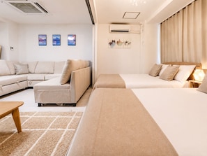 Ett modernt hotellrum med en soffa, två enkelsängar, ett träbord vid sängen, en luftkonditioneringsanläggning och konst på väggen.