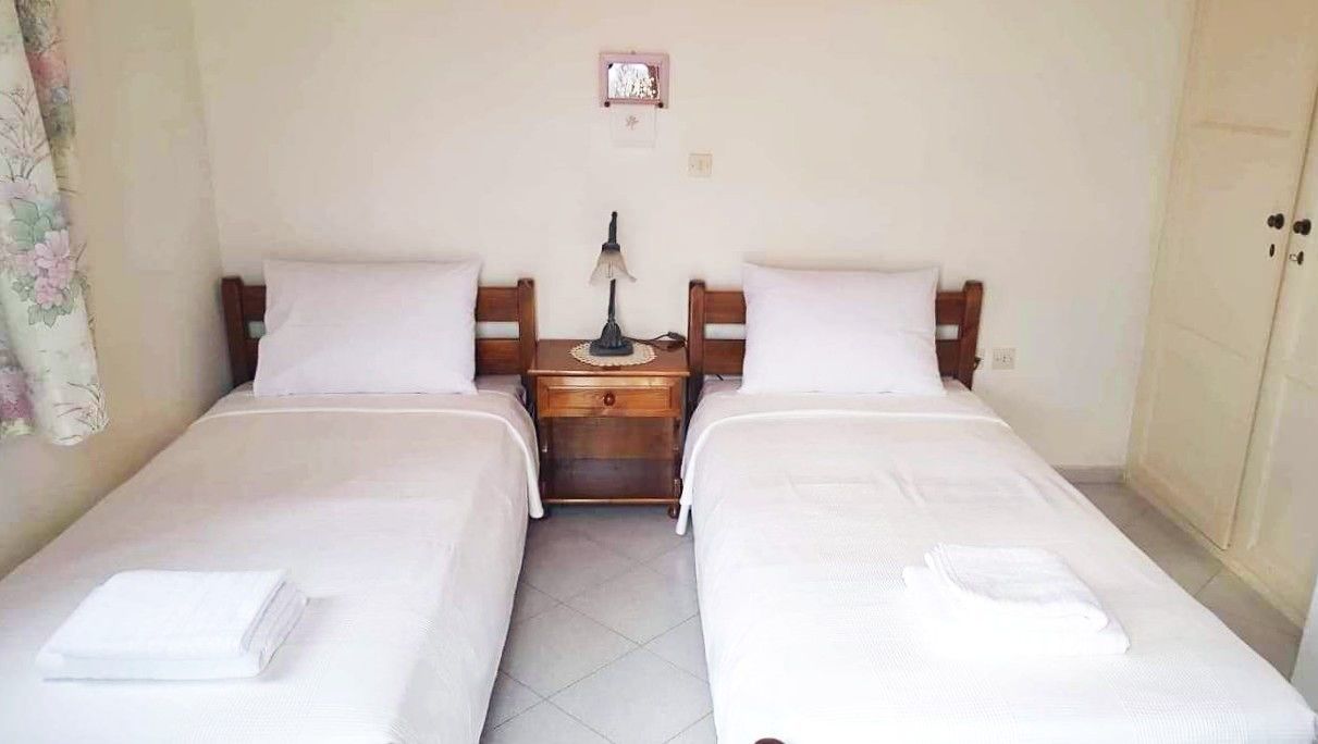 A twin room with two beds, a nightstand with a lamp, and a small window.