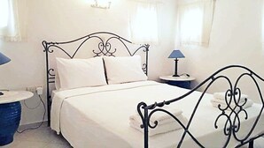 A neatly made bed with white linens, two bedside tables with lamps, and a large blue vase on the floor.