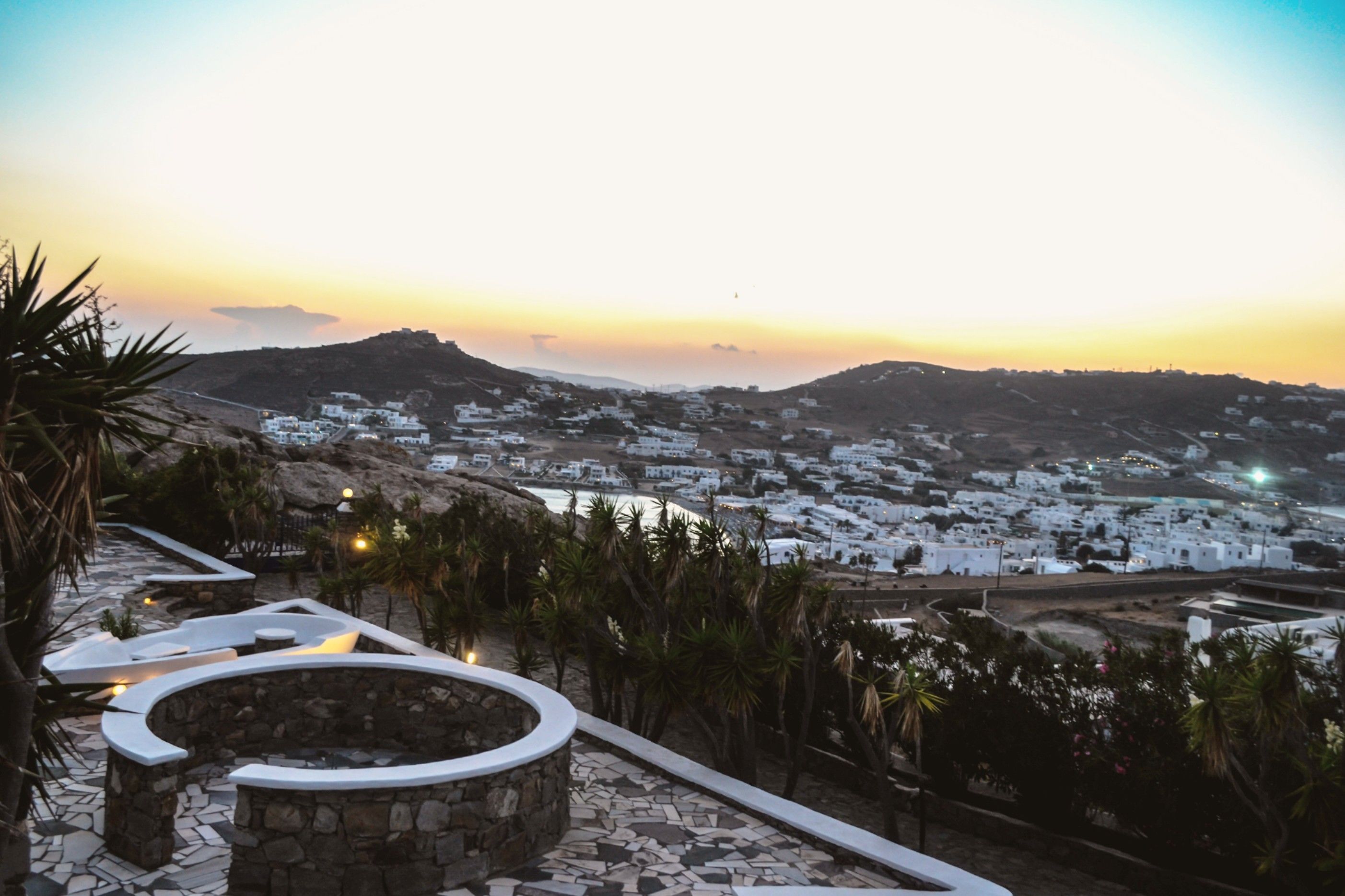Un pueblo costero con edificios blancos, un camino de piedra y vista al mar al atardecer.