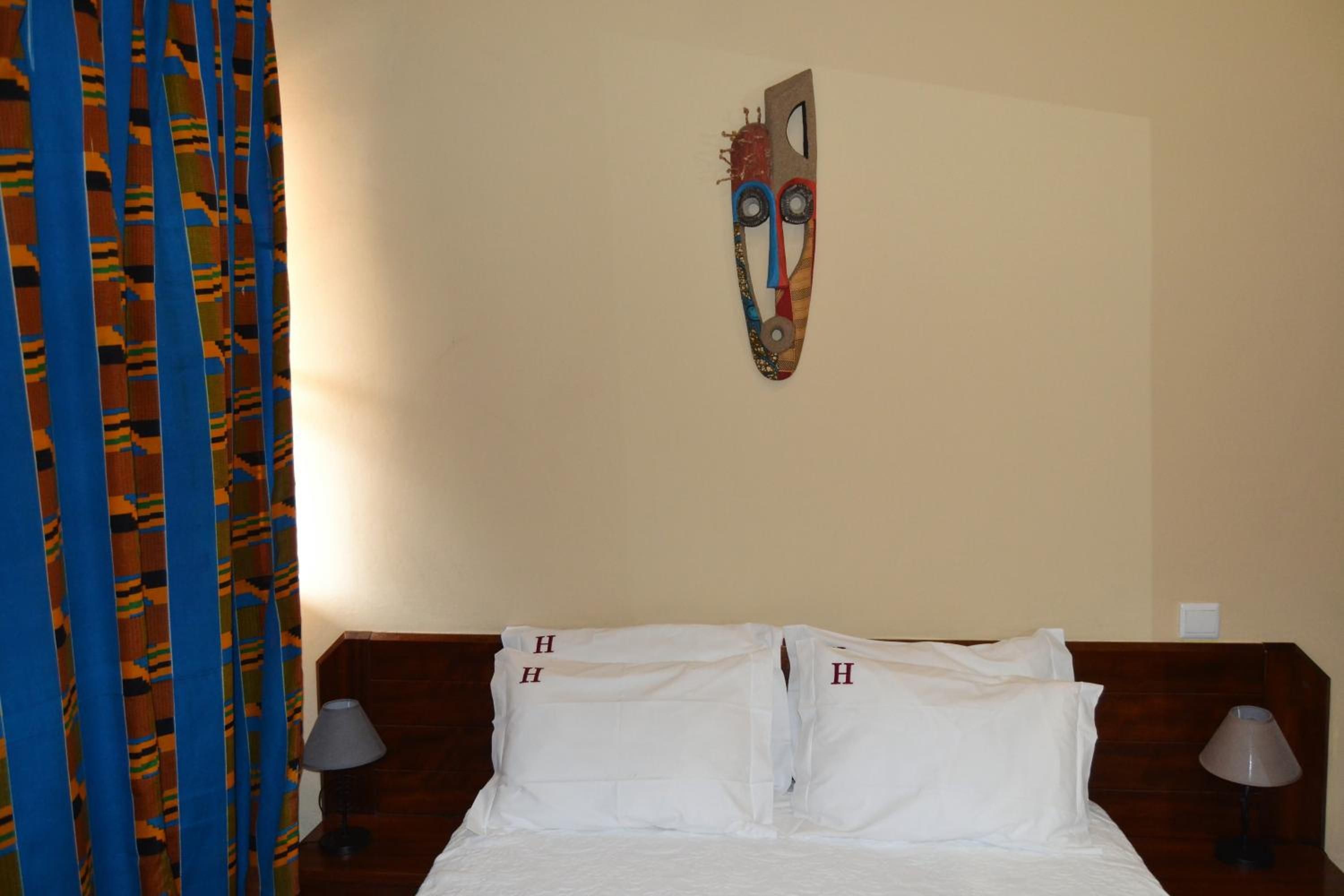 A hotel room with a bed, two bedside lamps, a patterned curtain, and a wall-mounted artwork.
